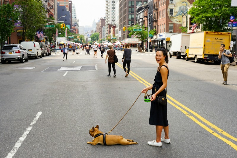 dog on leash laying on asphalt with owner laughing at camera