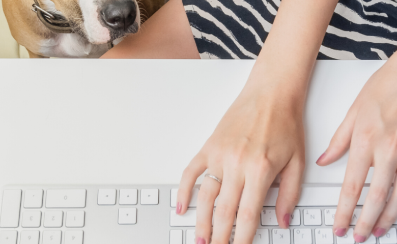 overhead view of dog staring up at female owner while she types on keyboard, caption reads "working from home with your dog"