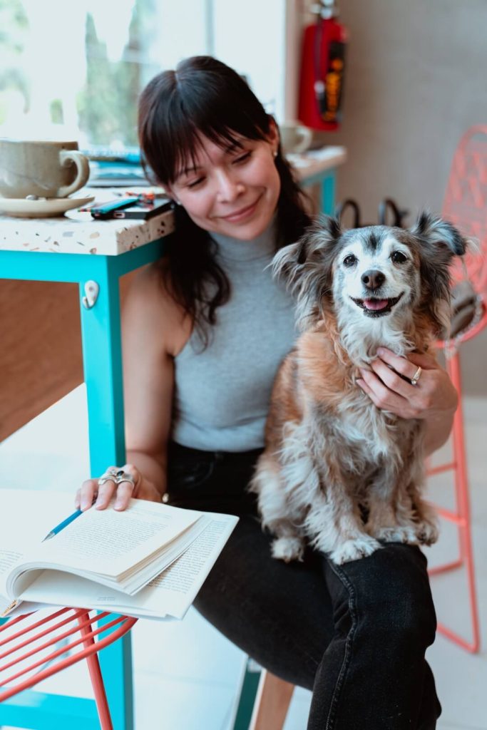 woman holding book in one hand and dog in lap