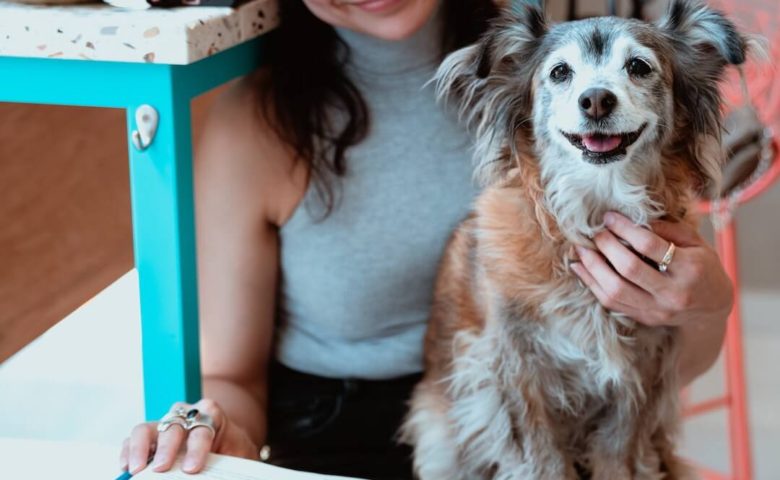 woman holding book in one hand and dog in lap