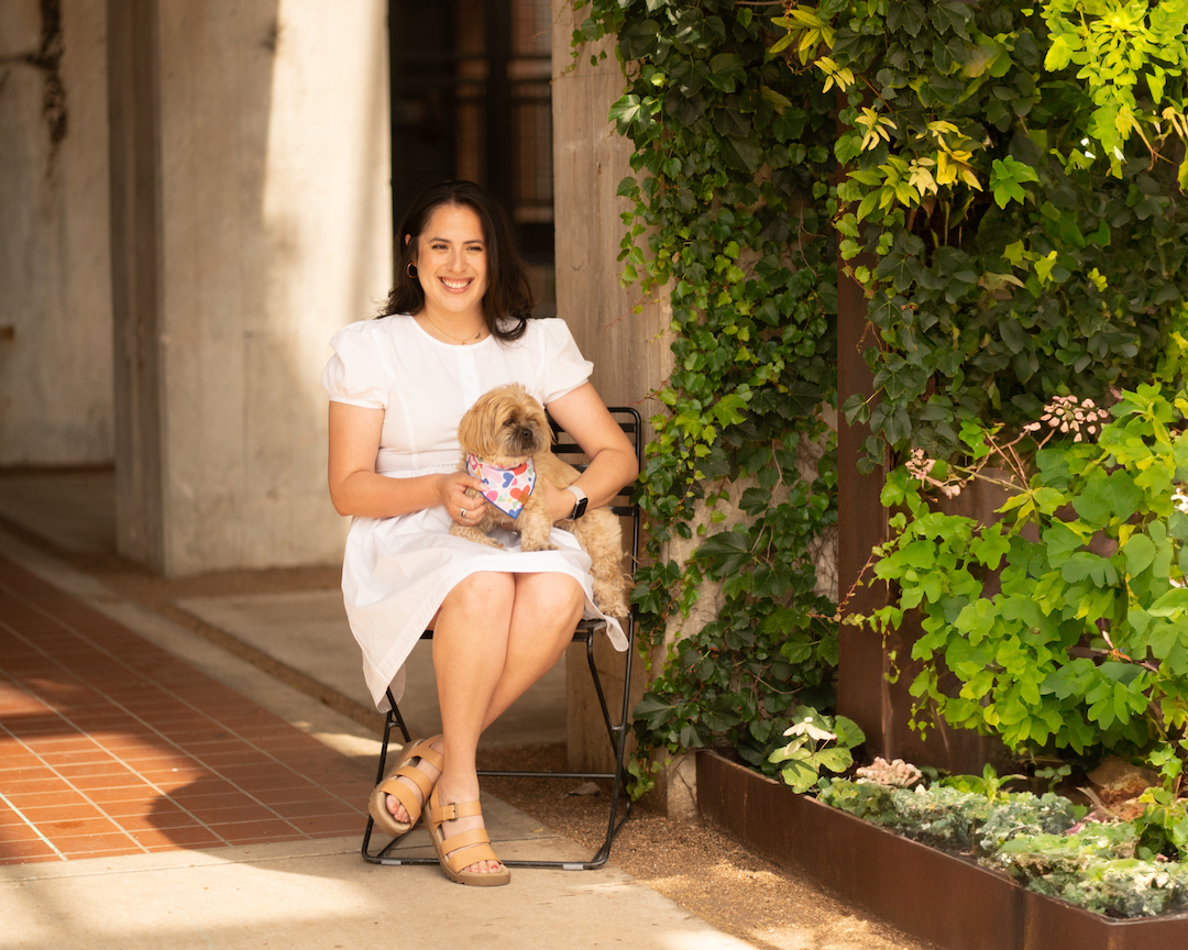 Hispanic woman in white dress sitting in chair by green ivy with a Shitzu dog in her lap